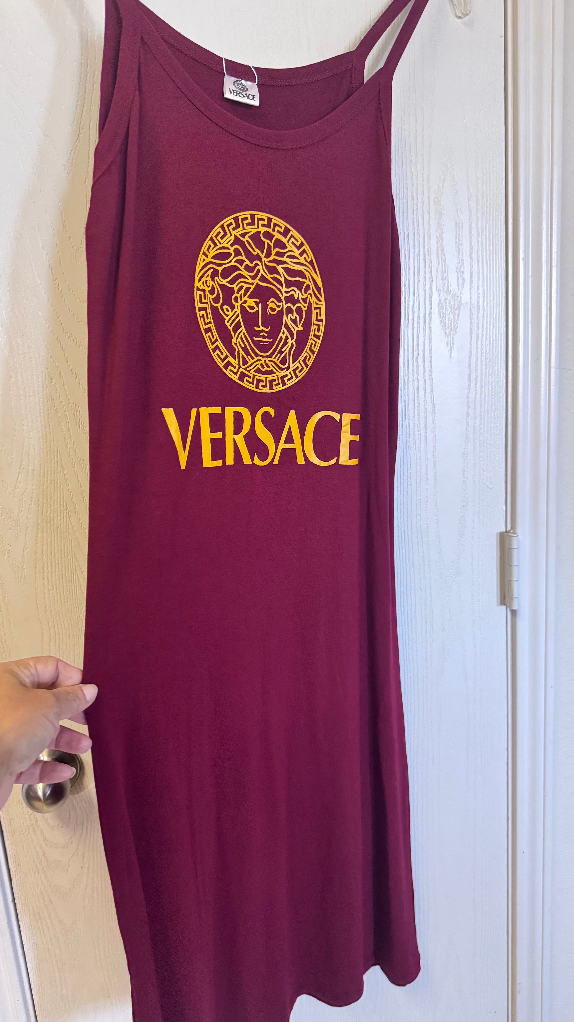 Maroon tank top with gold Versace logo held against a white door.