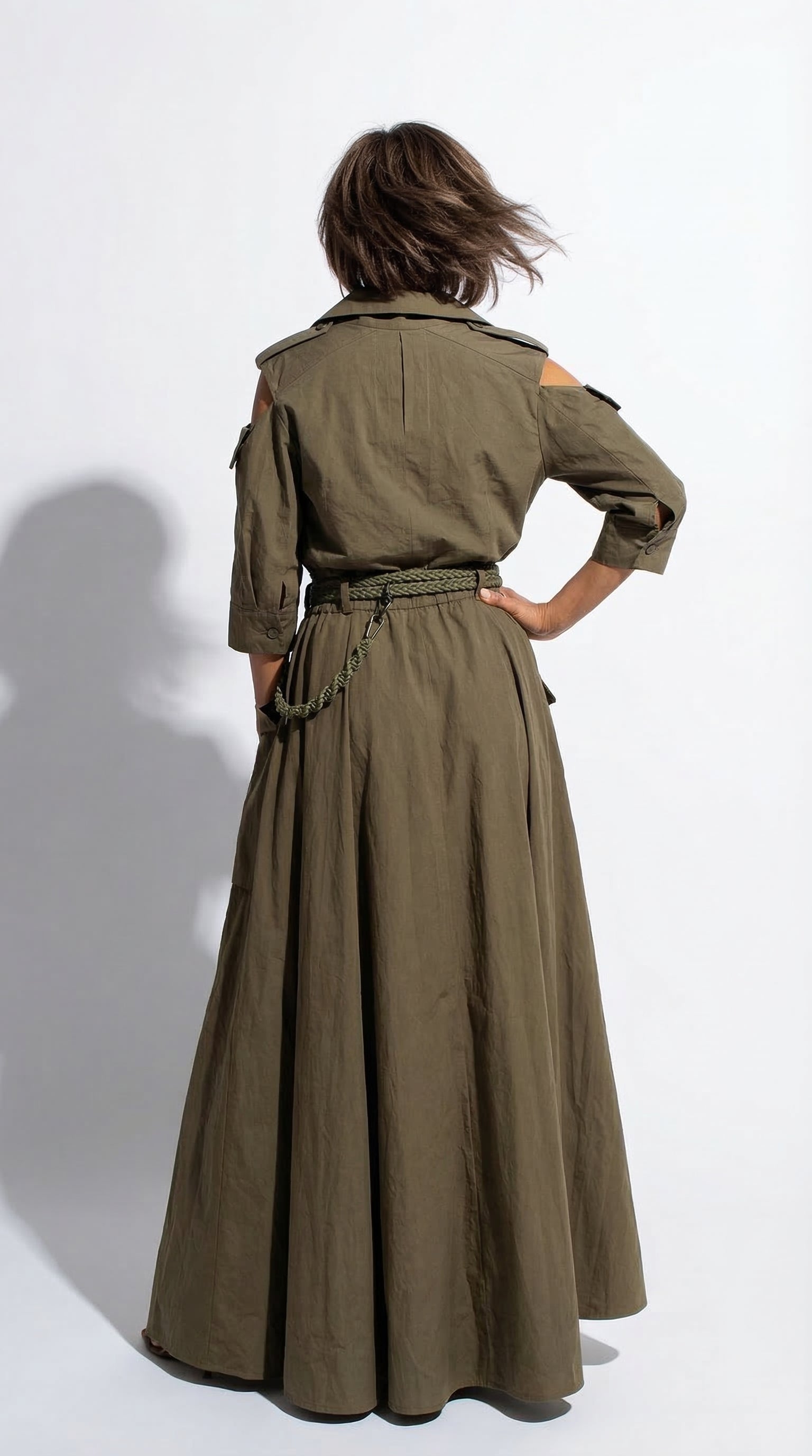Person wearing a long olive green dress with a belt on a white background