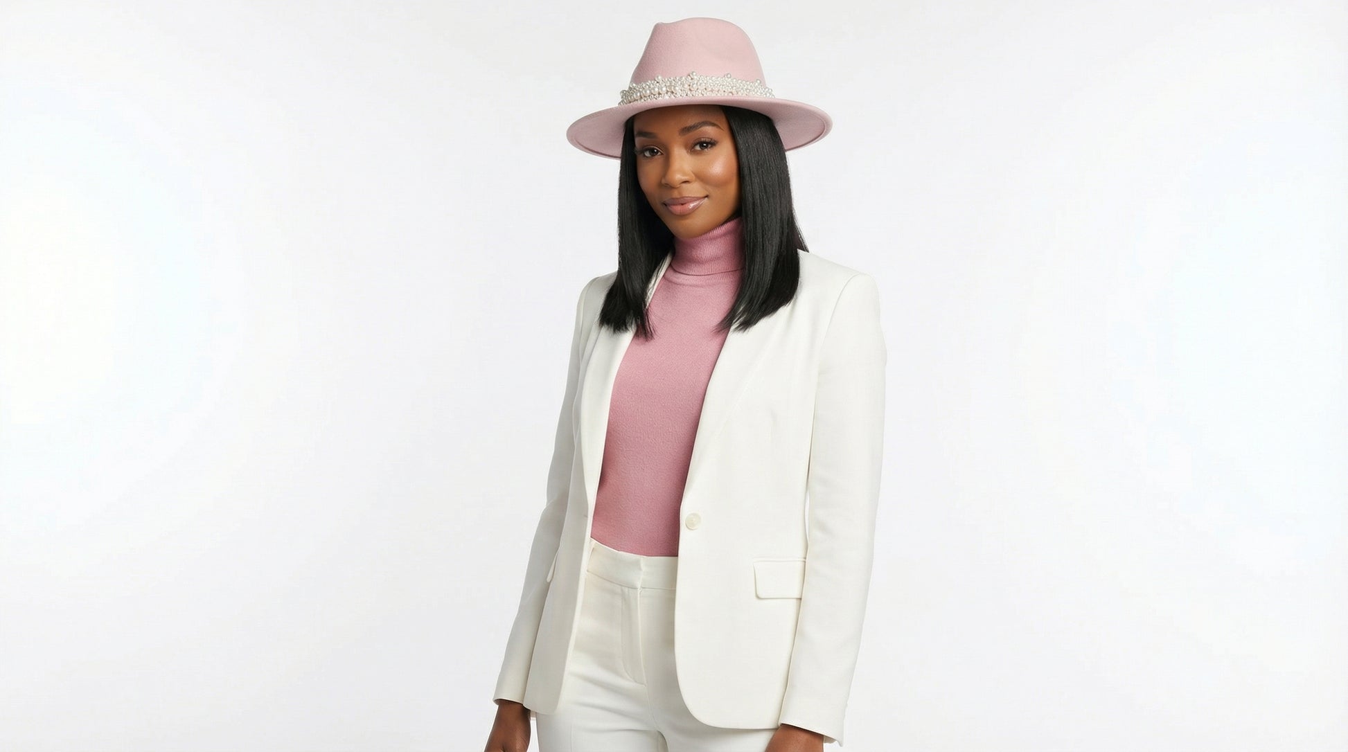 Woman wearing a white blazer, pink top, and pink hat on a white background