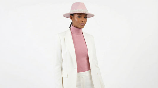 Woman wearing a white blazer, pink sweater, and pink hat on a white background