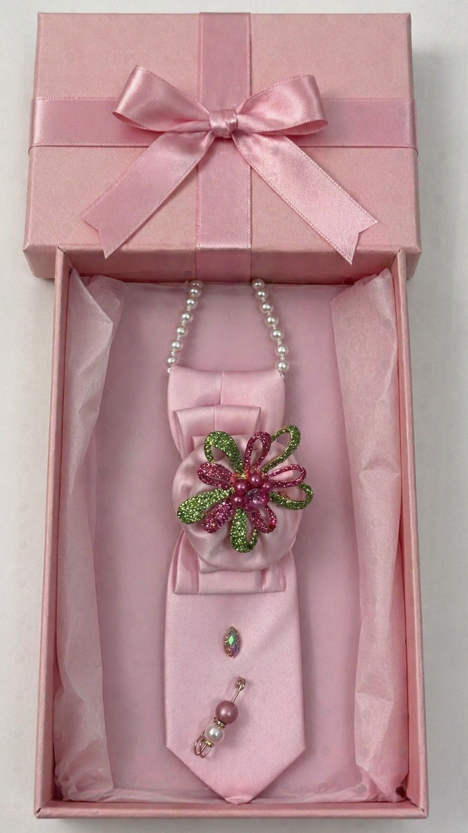 Pink bow tie with decorative brooch and necklace in a pink box on a white background