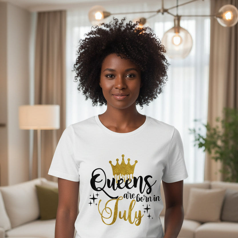 White t-shirt with 'Queens are born in July' text and gold crown design on a light wooden surface.