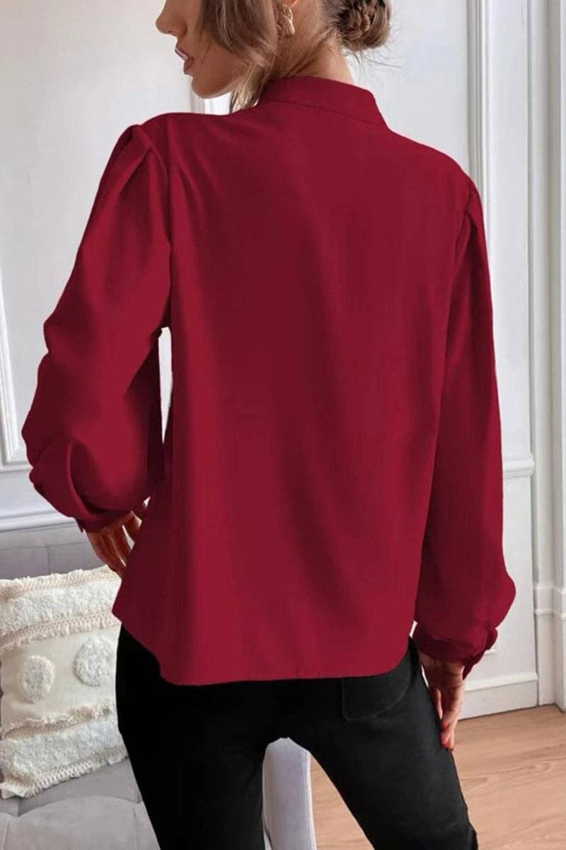 Person wearing a red blouse with a bow detail on the back, standing in a room.