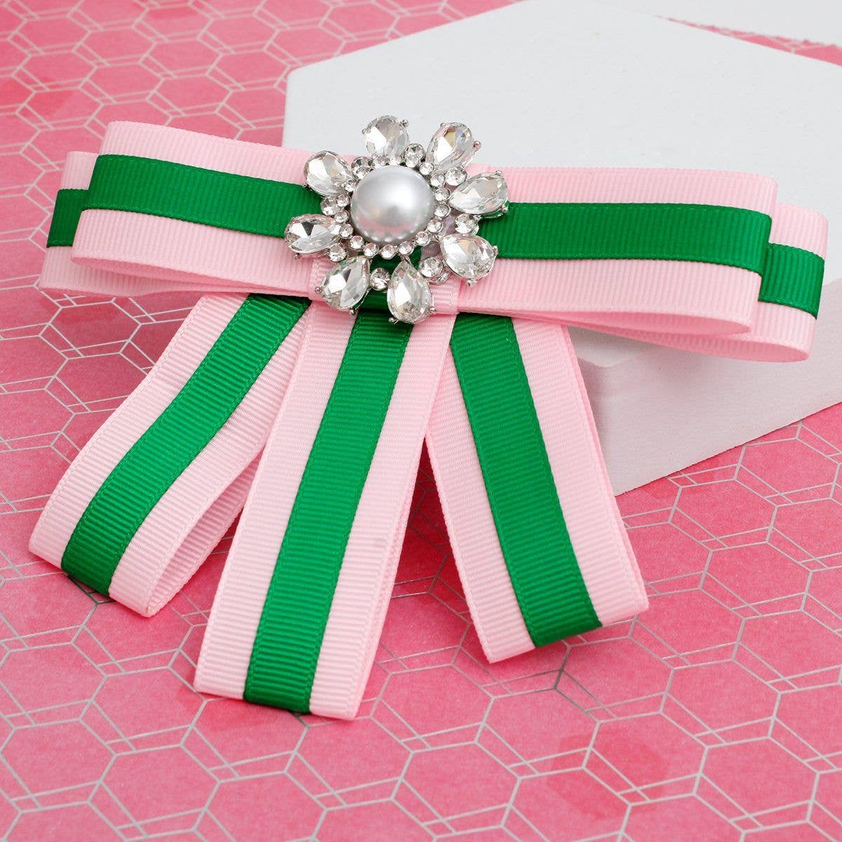 Bow with pink and green ribbons and a decorative brooch on a pink background