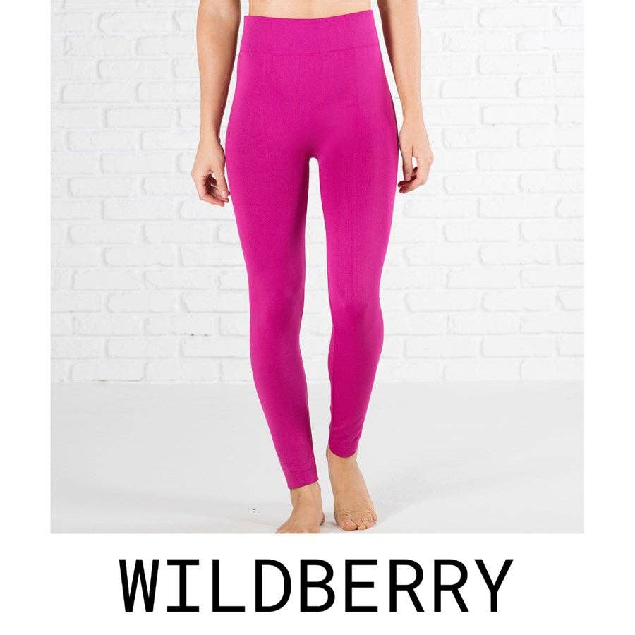 Person wearing bright pink leggings against a white brick wall with 'Wildberry' branding.