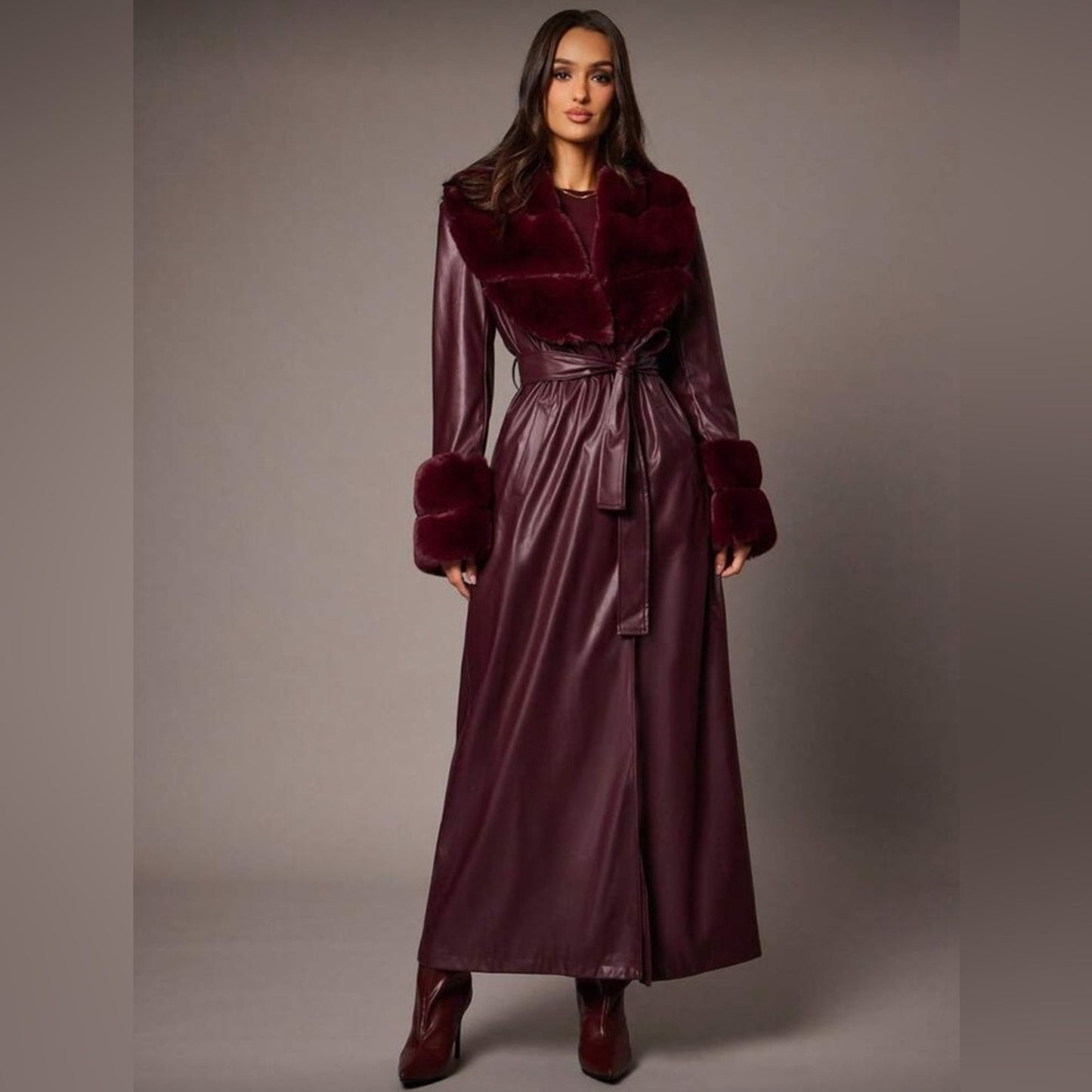Woman wearing a burgundy coat with fur trim on a plain background