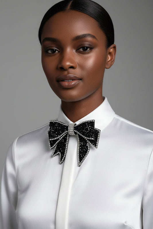 Black bow-shaped brooch with rhinestones held by a hand against a neutral background