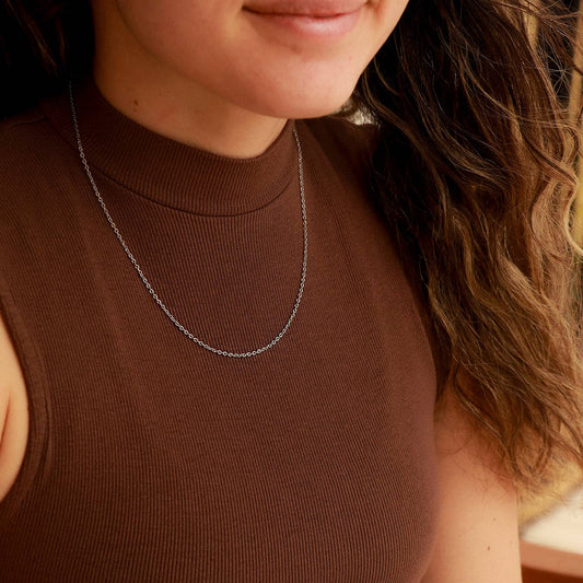 Close-up of a person wearing a brown top and a silver necklace.