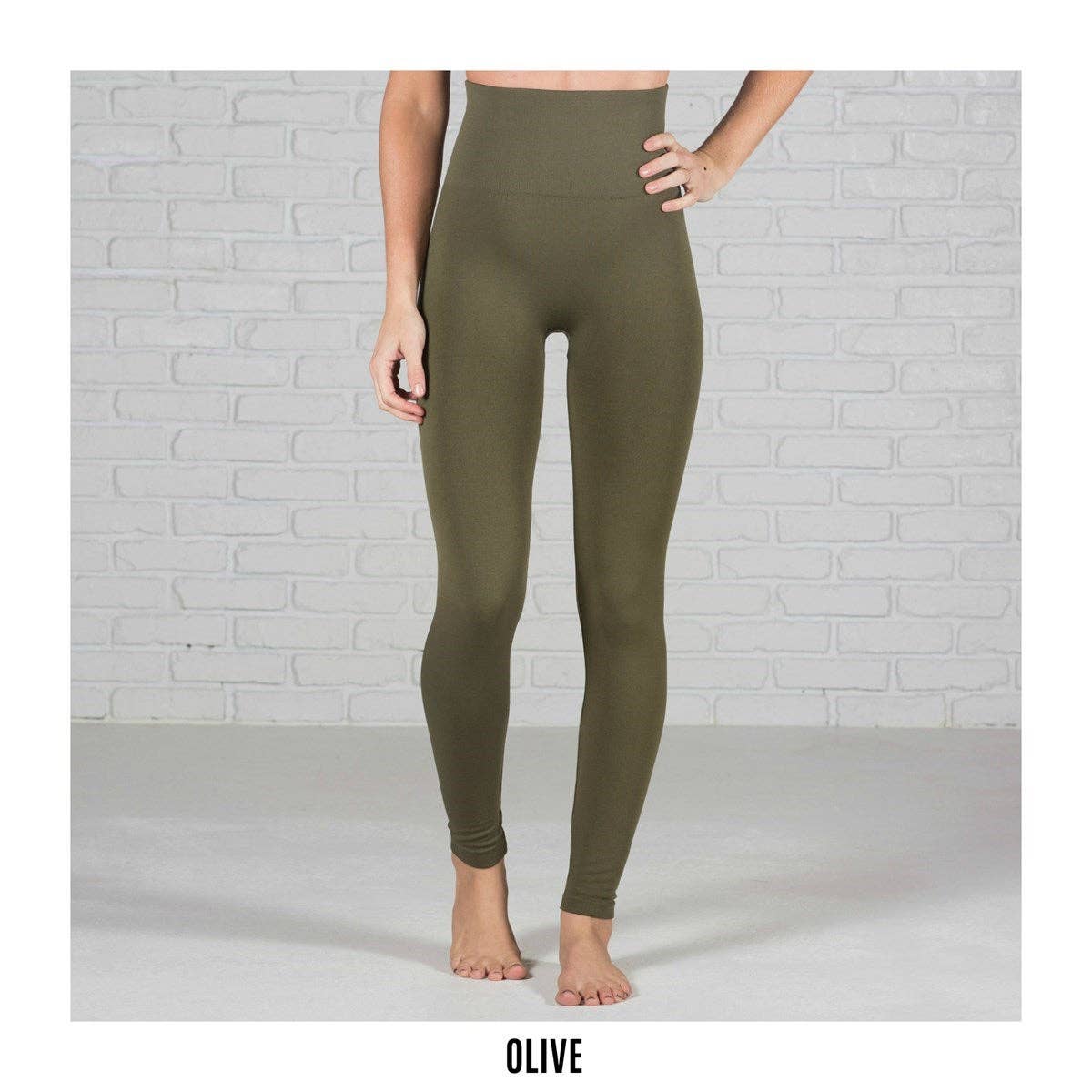 Olive green leggings worn by a person against a light gray brick wall.