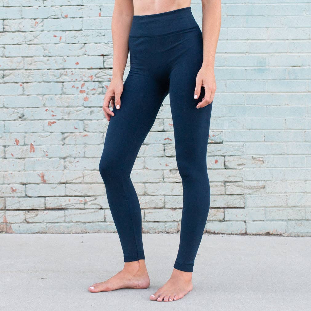 Person wearing navy leggings standing against a light blue brick wall.