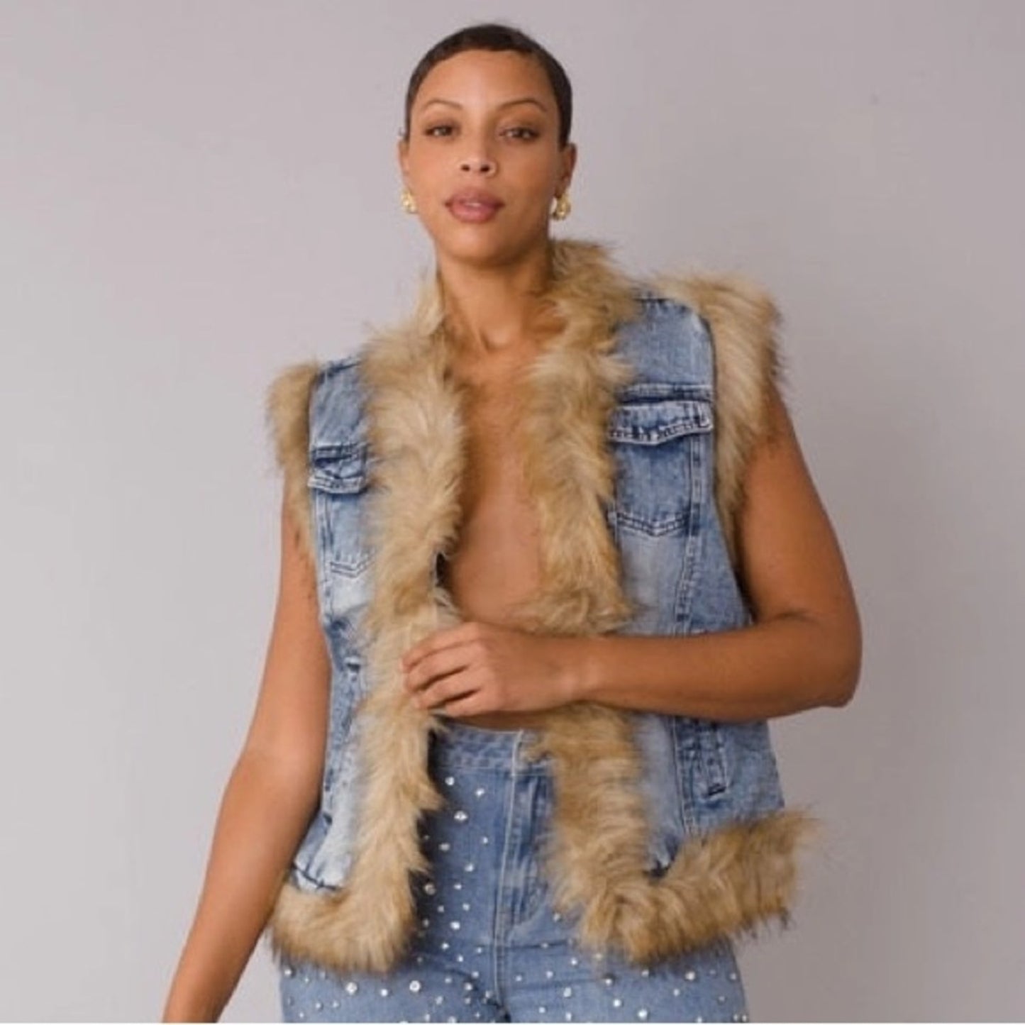 Woman wearing a denim vest with fur trim against a plain background