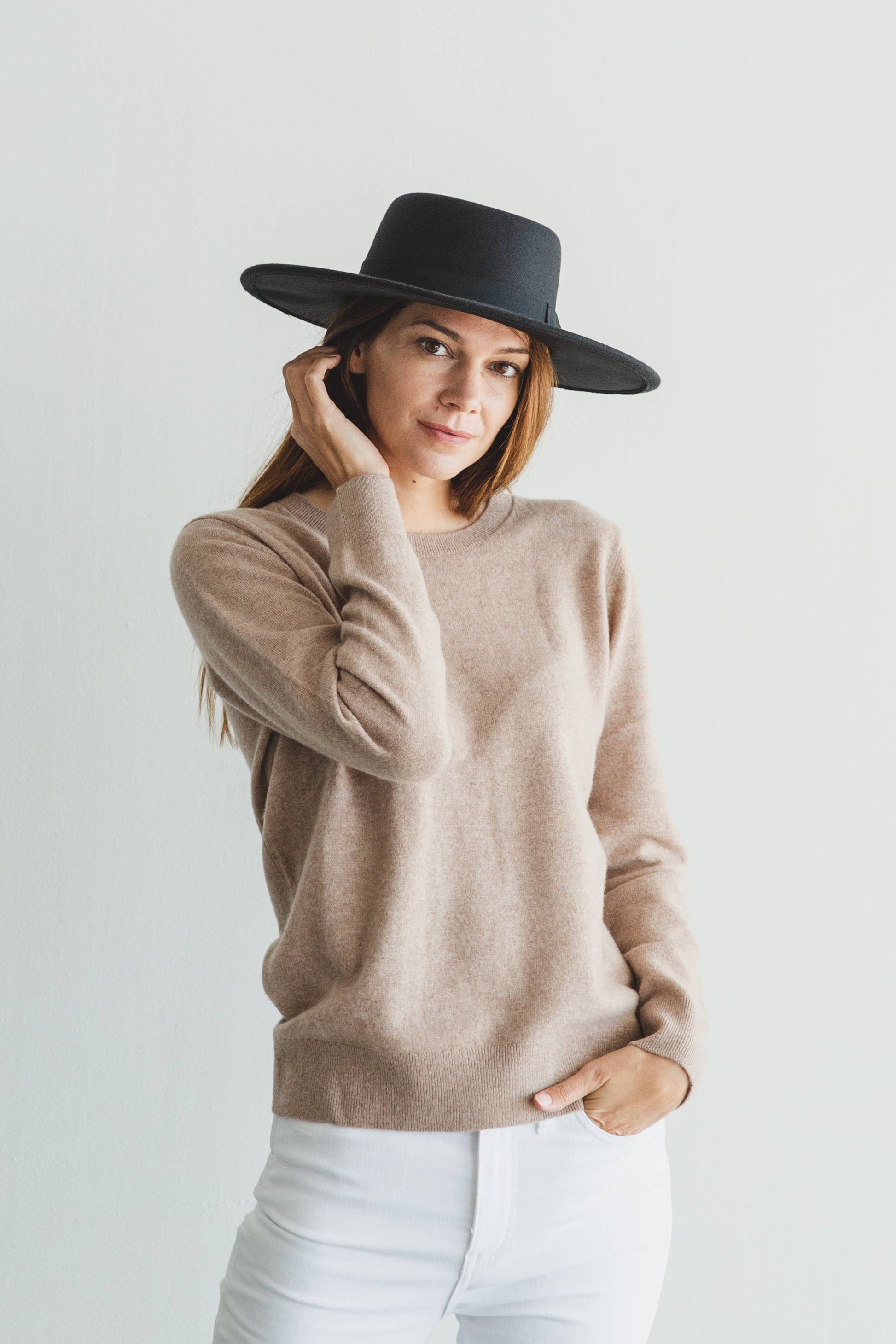 Woman wearing a beige sweater and black hat against a white background