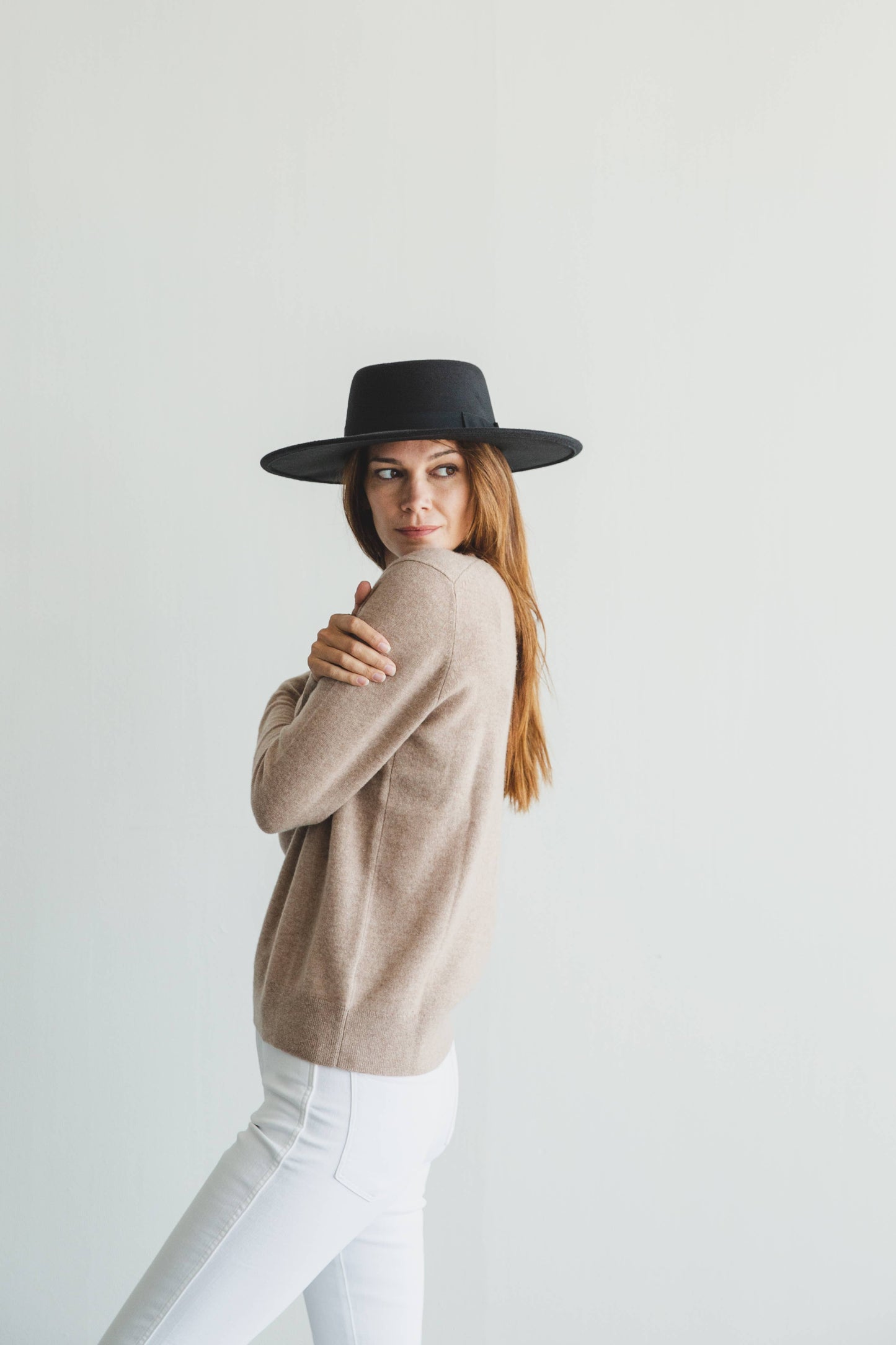 Woman wearing a beige sweater and black hat against a white background