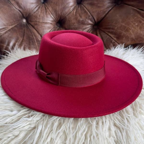Red hat with a wide brim on a white fur surface with a brown leather couch in the background