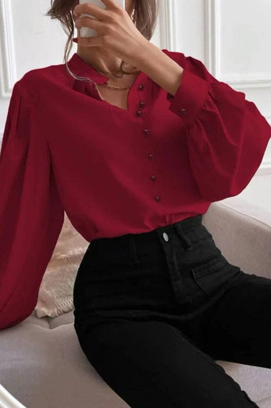 Person wearing a red blouse with puffed sleeves and black pants sitting on a couch.