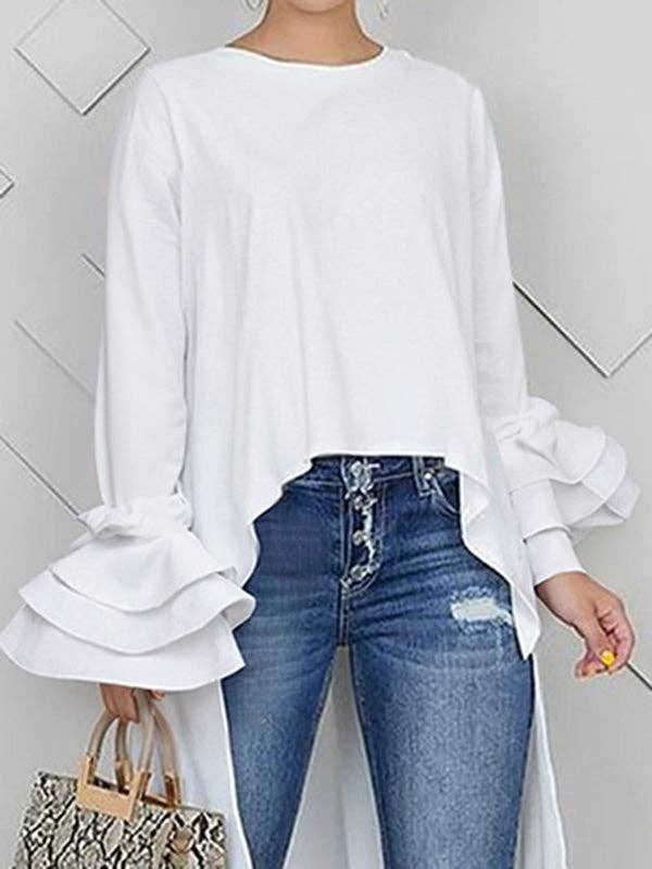 Person wearing a white blouse with ruffled sleeves and blue jeans, holding a patterned handbag.