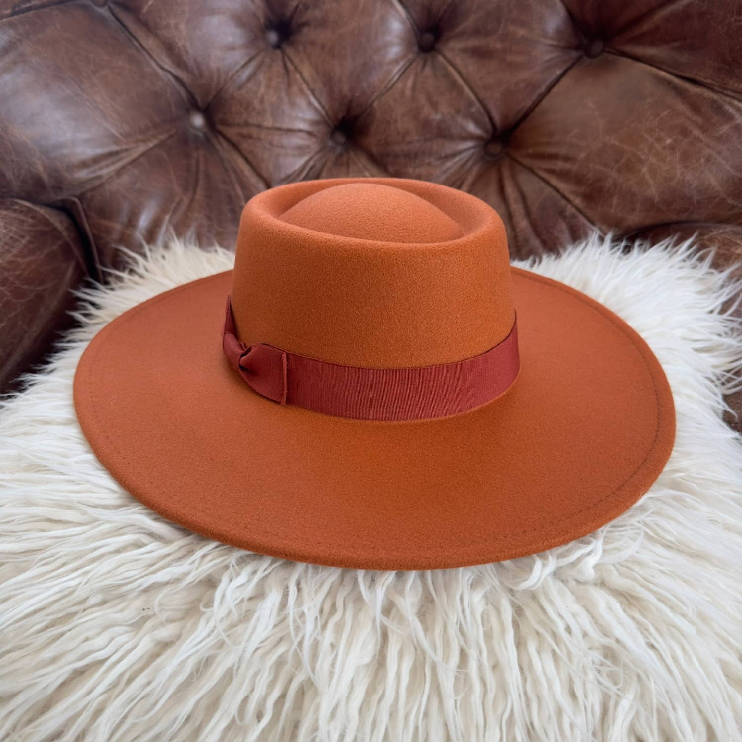 Orange hat with a red band on a white furry surface with a brown leather couch in the background