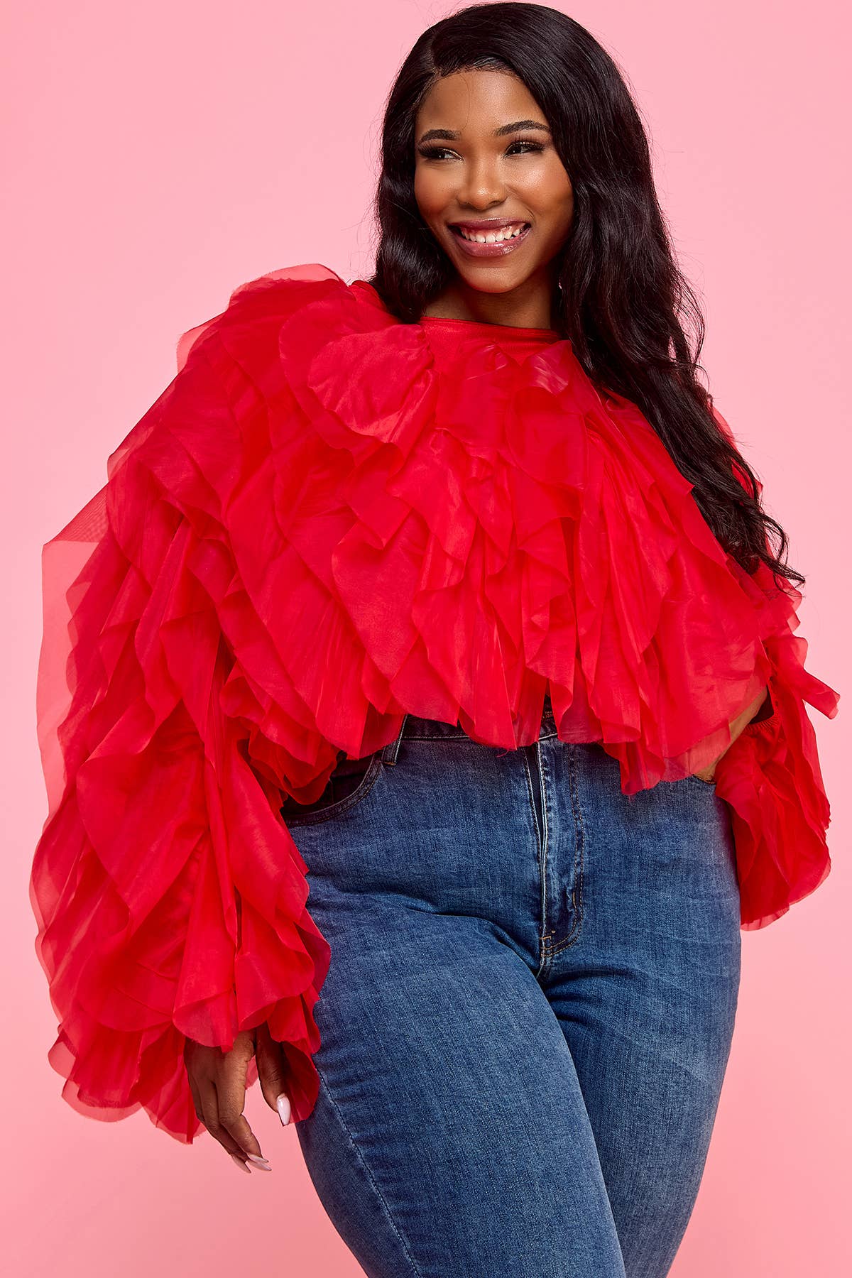 Woman wearing a red ruffled top and blue jeans on a pink background