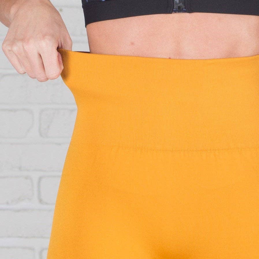 Person holding a mustard yellow fabric against a white brick wall.