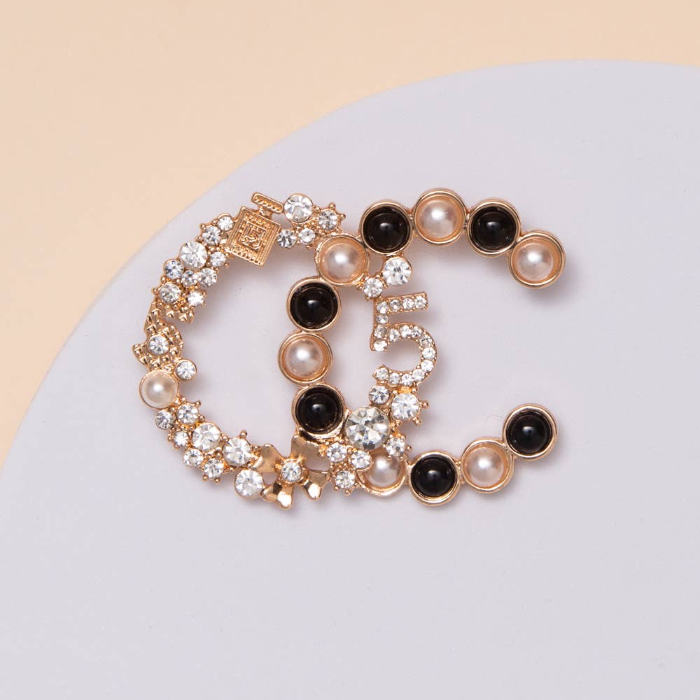 Two gold bracelets with pearls and black stones on a light gray surface.