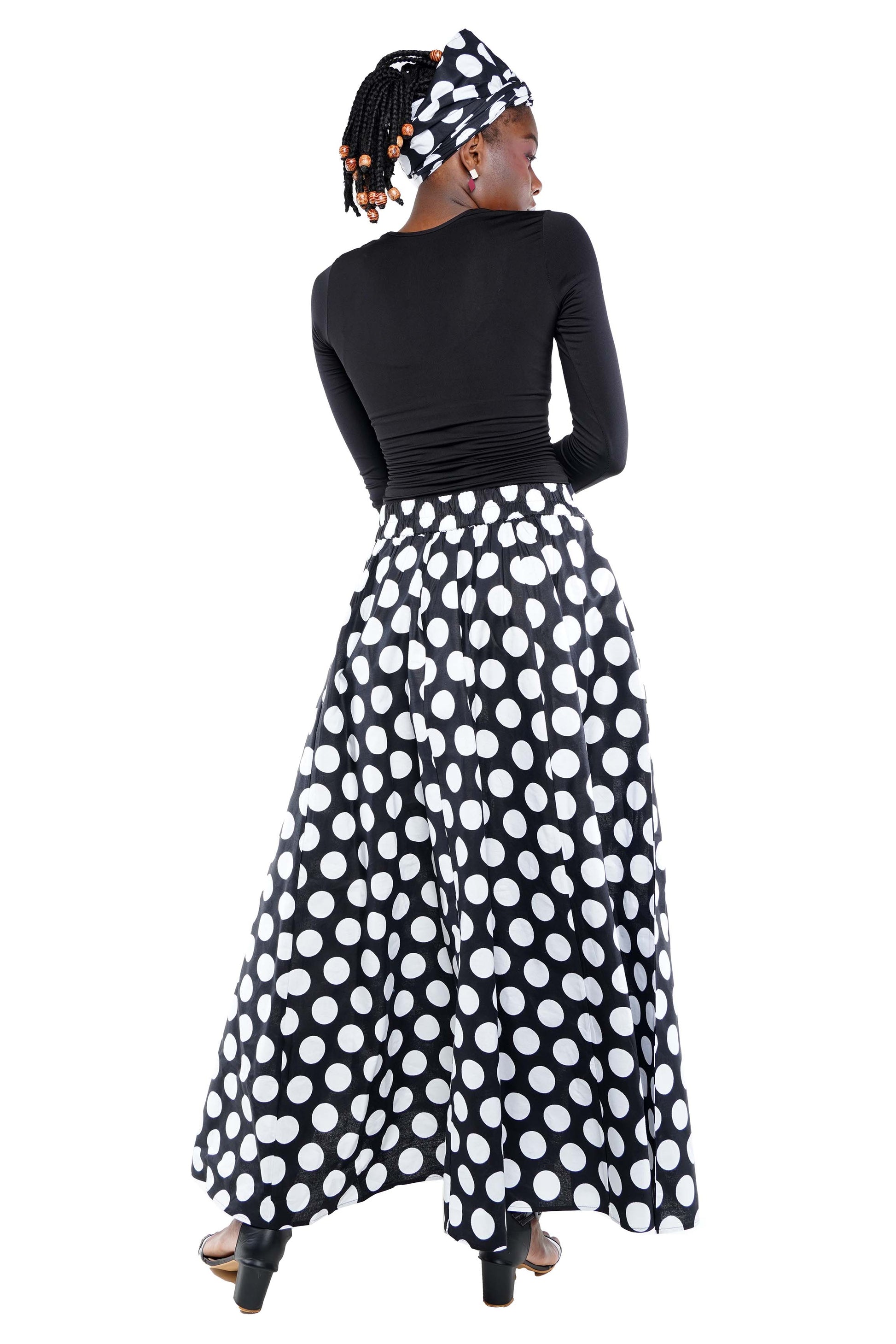 Woman wearing a black top and polka dot skirt with a headscarf on a white background