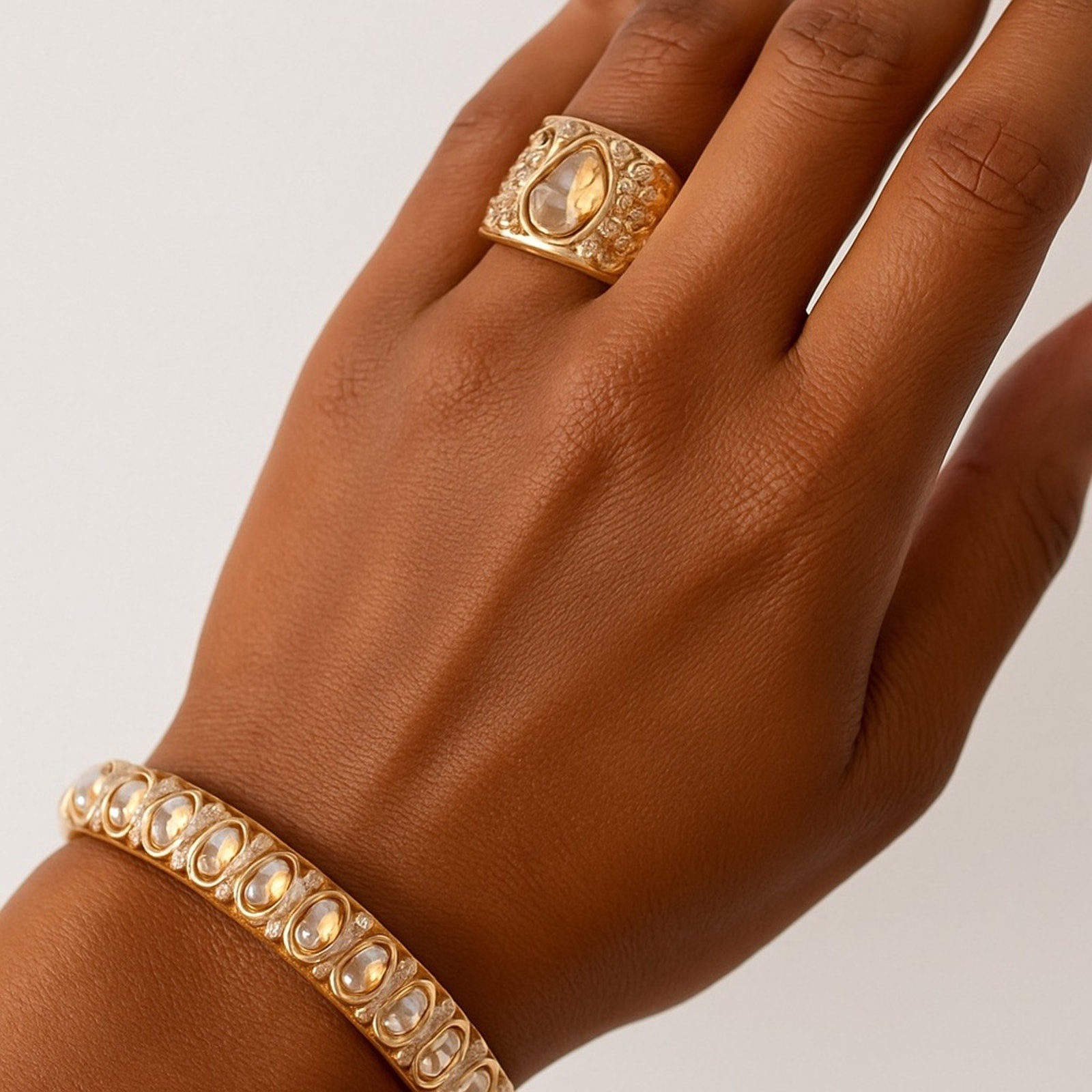 Hand wearing a gold ring and bracelet on a neutral background