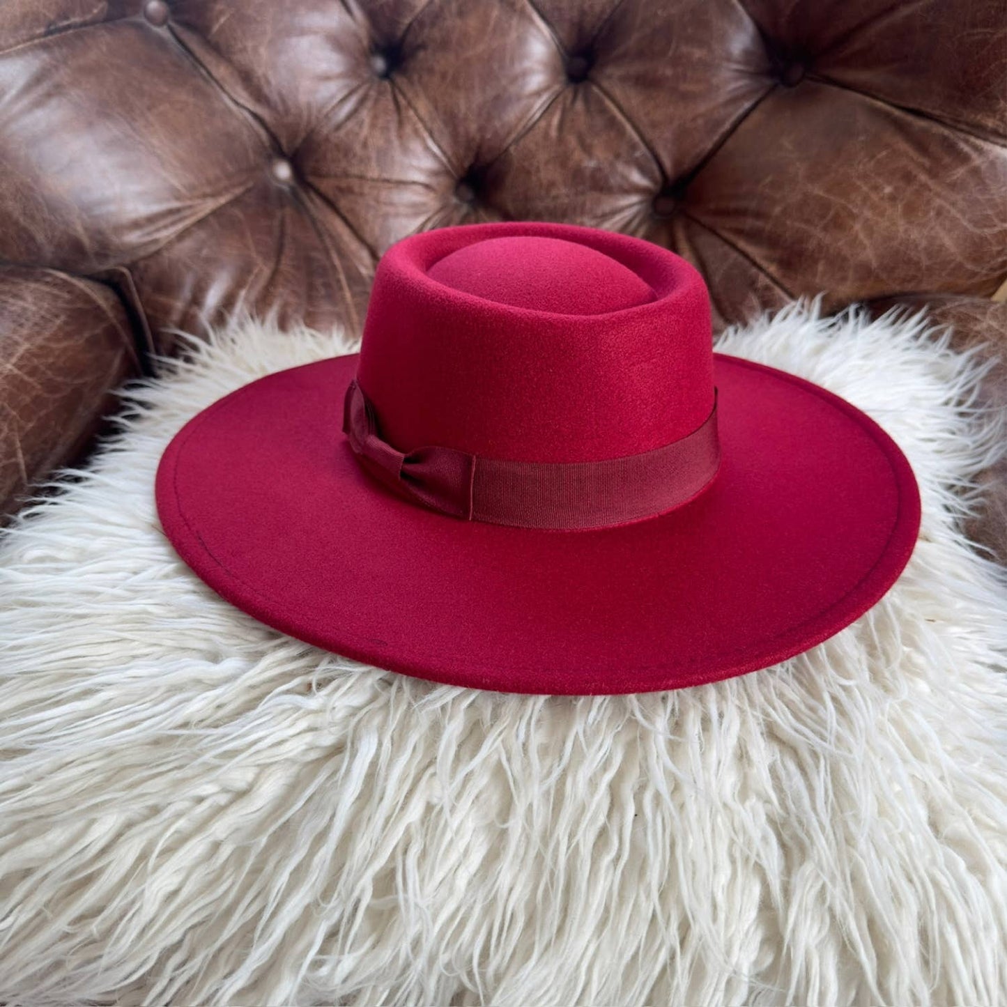 Red hat on a fluffy white surface with a brown leather couch in the background