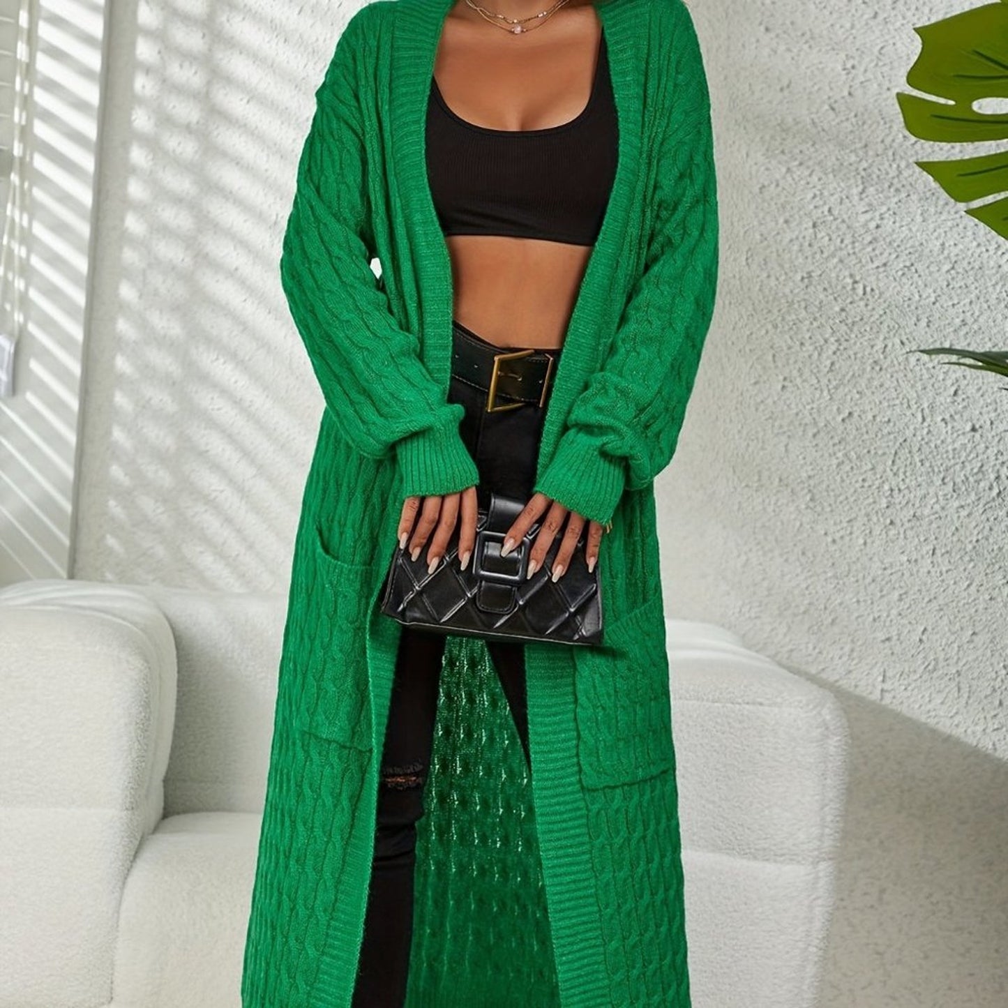Person wearing a long green cardigan holding a black handbag indoors.