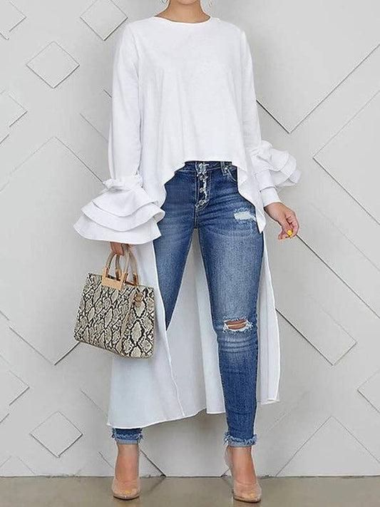 Person wearing a white long-sleeve top and blue jeans, holding a patterned handbag against a white geometric background.