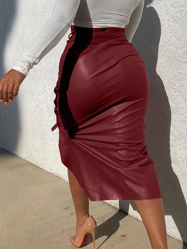 Person wearing a burgundy leather skirt with a white top against a light gray wall.
