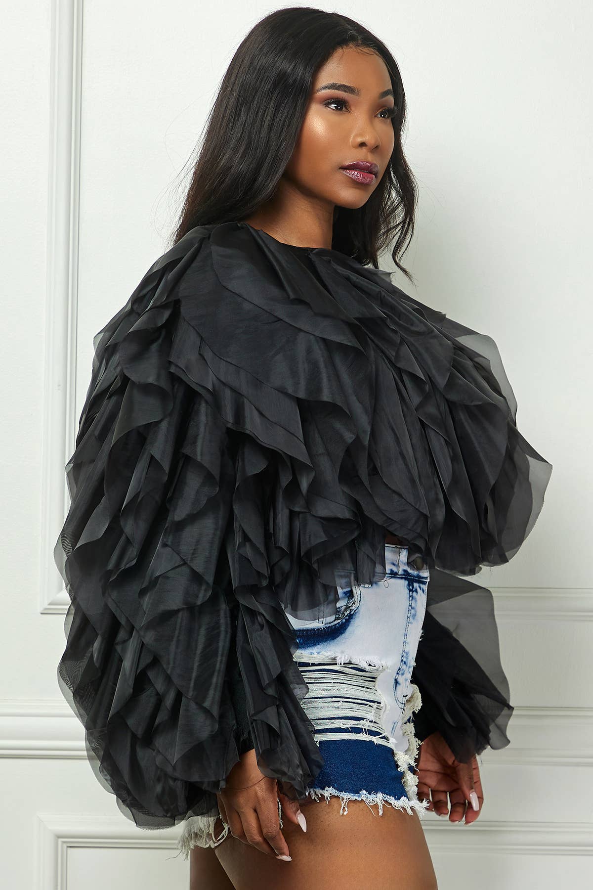 Woman wearing a black ruffled top with a white wall background