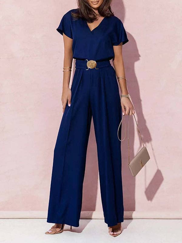 Woman wearing a navy blue jumpsuit with a belt against a pink background