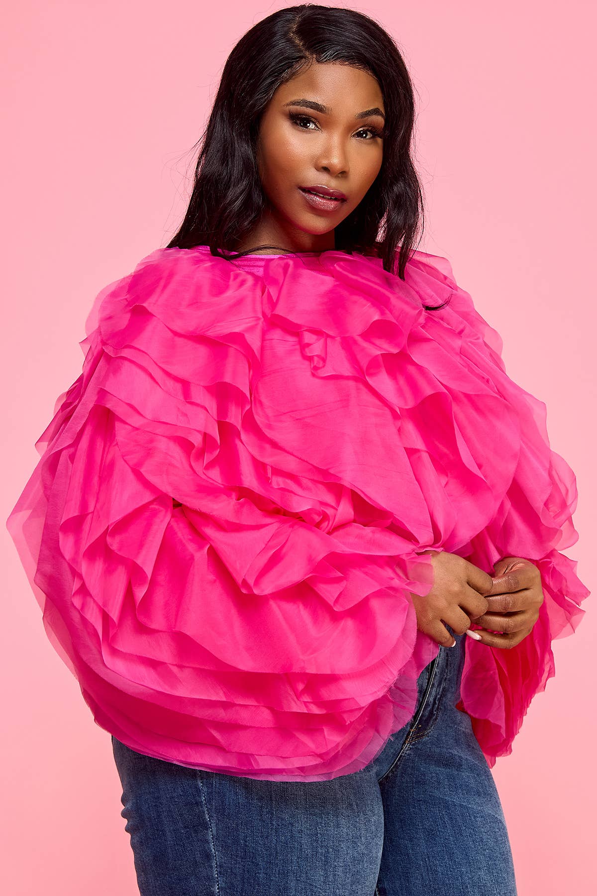 Woman wearing a bright pink ruffled top against a pink background