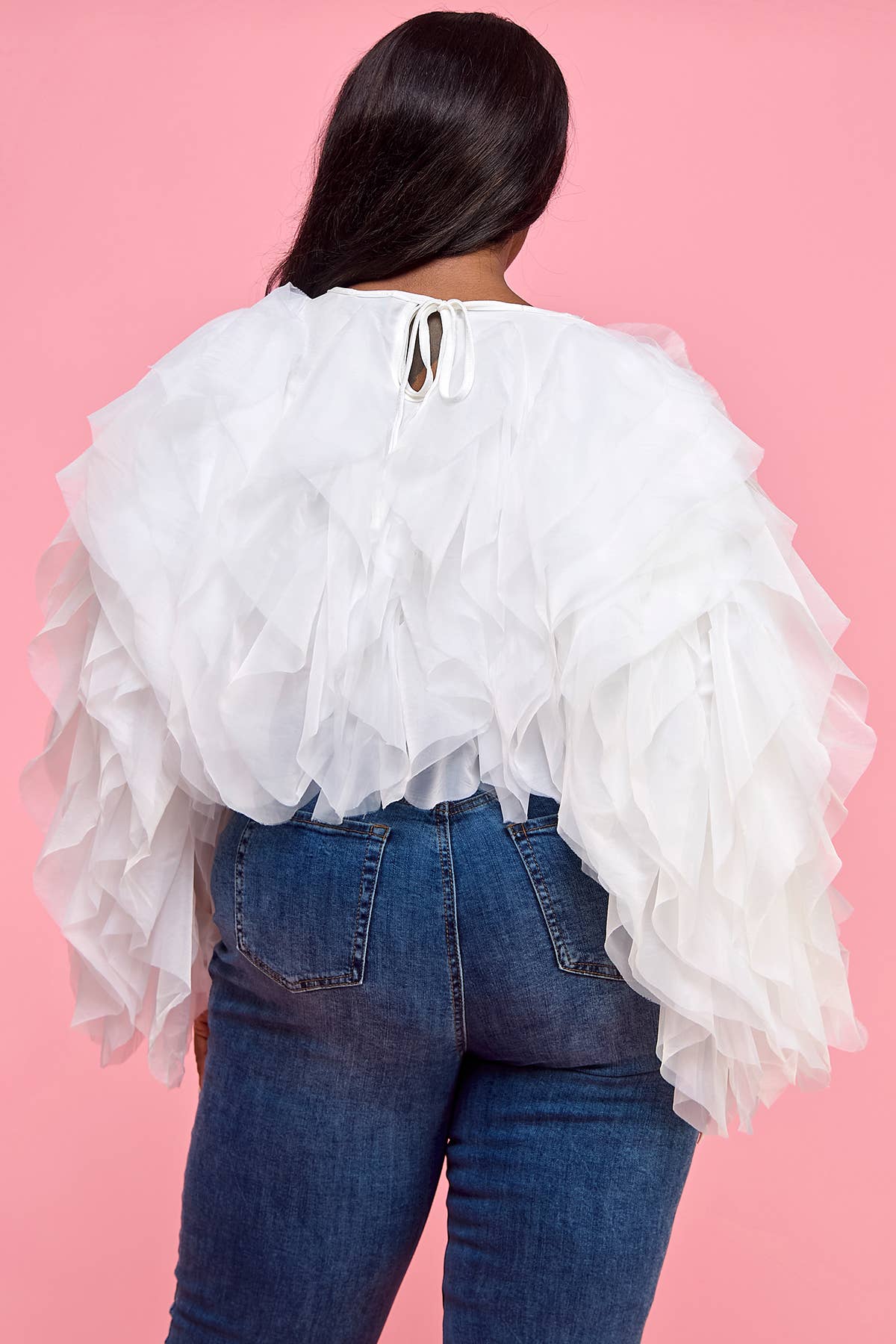 Person wearing a white ruffled blouse and blue jeans on a pink background