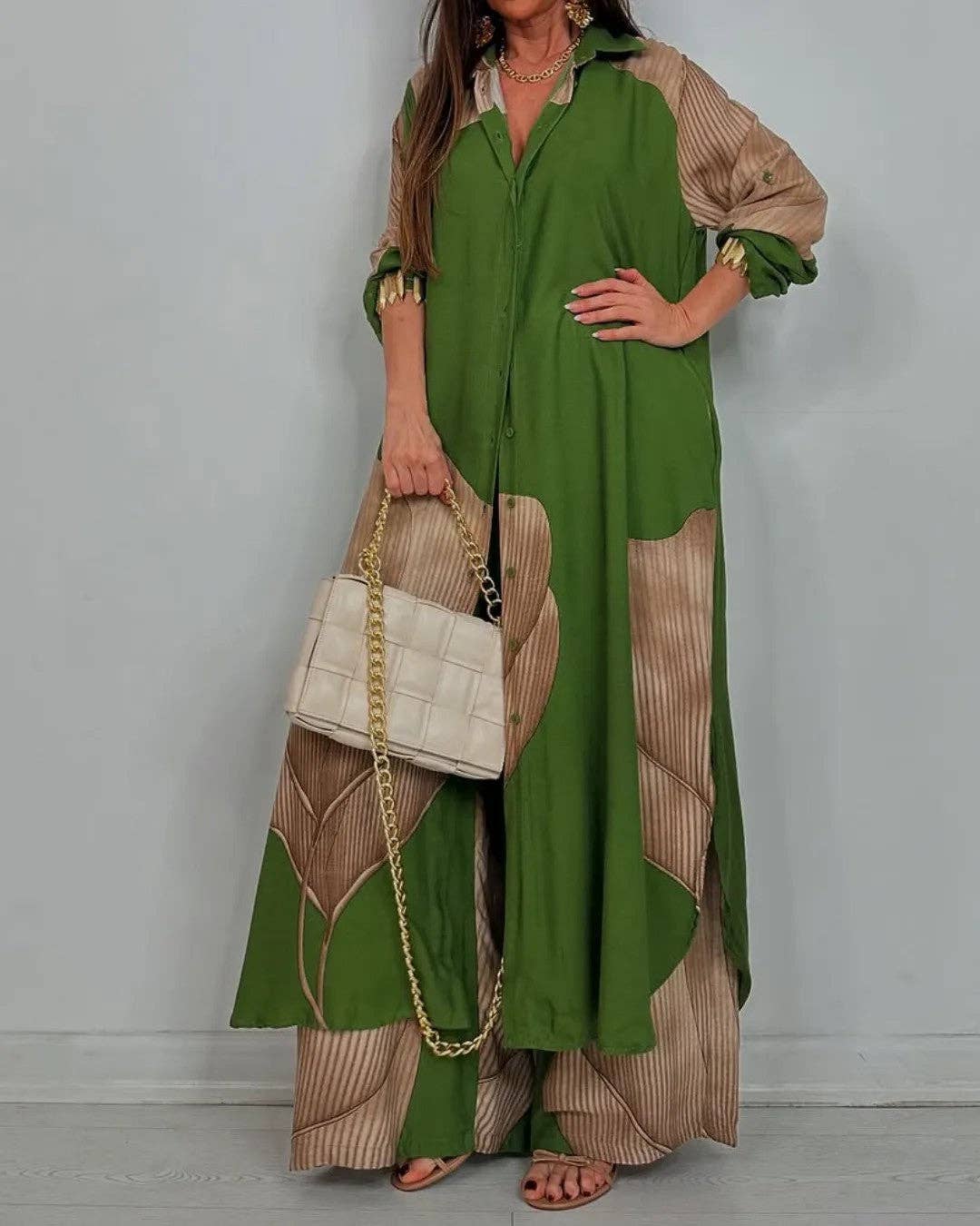 Woman wearing a green and beige dress holding a beige handbag against a plain background