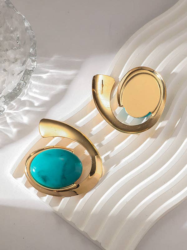 Gold earrings with turquoise stones on a textured white surface