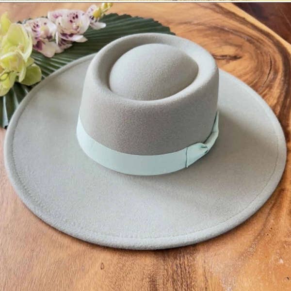 Light gray wide-brimmed hat on a wooden surface with flowers in the background