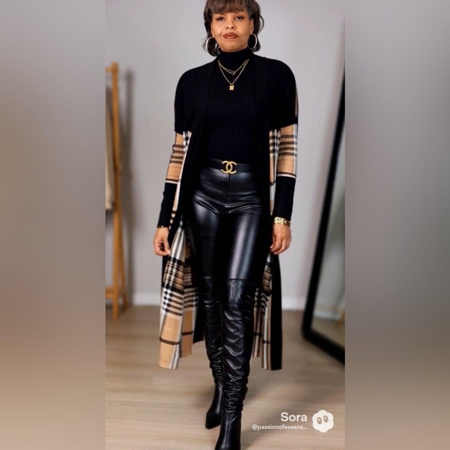 Person wearing a black outfit with plaid sleeves and leather pants in a neutral setting.