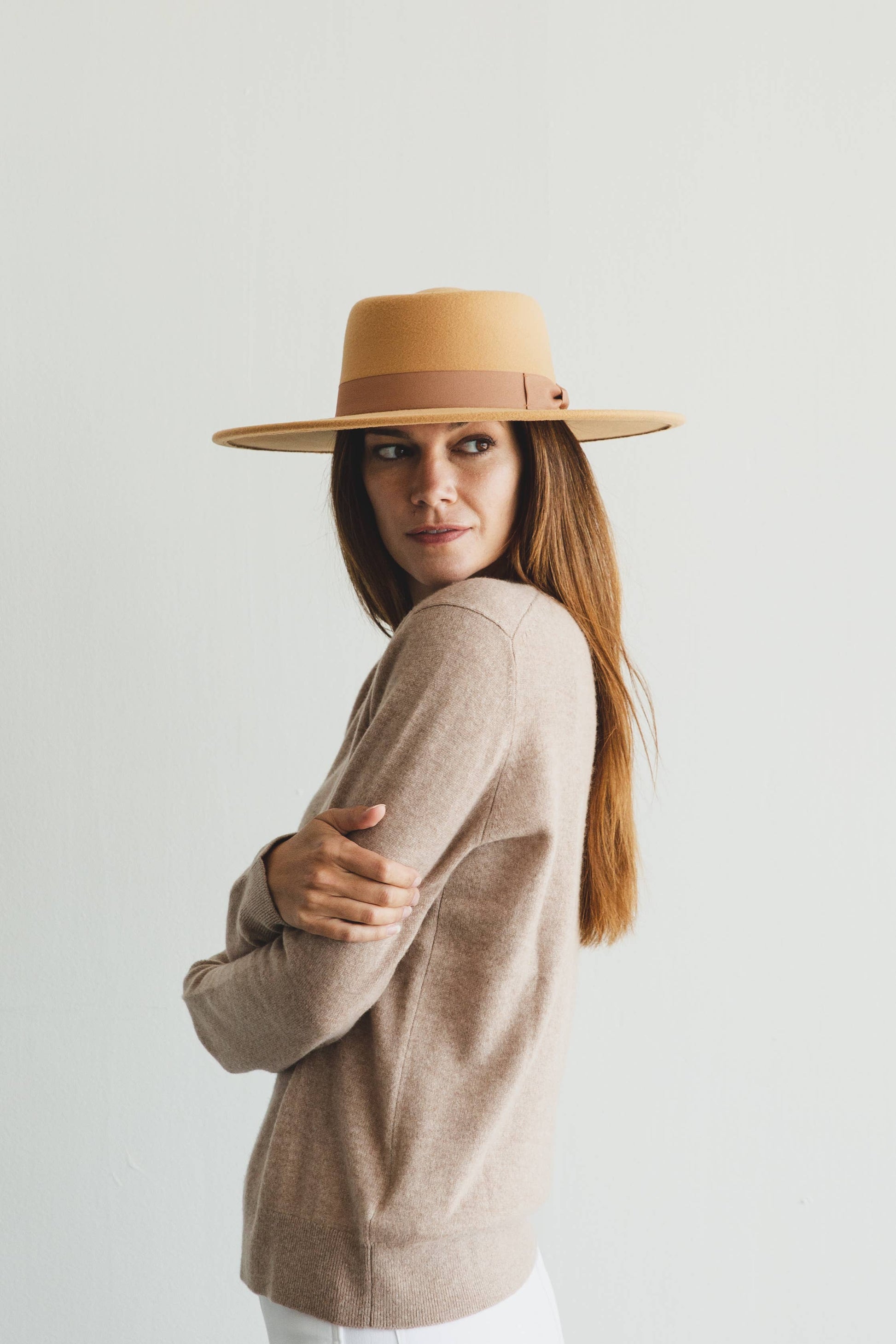 Woman wearing a beige hat and sweater against a plain background