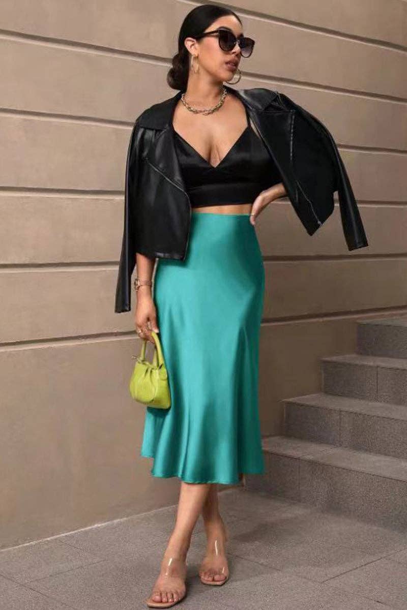 Woman in black jacket and teal skirt standing on steps with a beige wall background