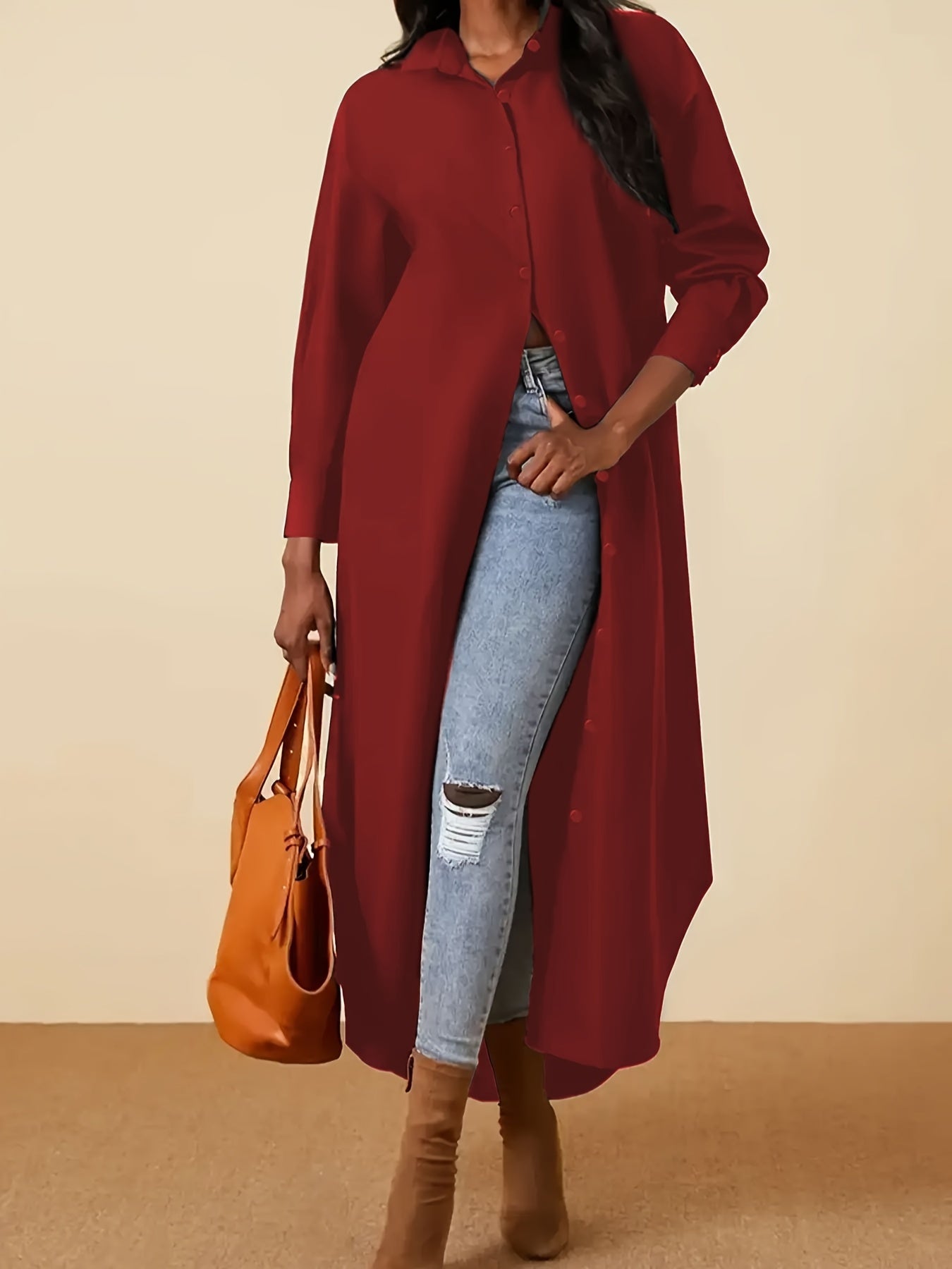 Person wearing a long burgundy coat, light blue jeans, and brown boots, holding an orange handbag on a beige background.