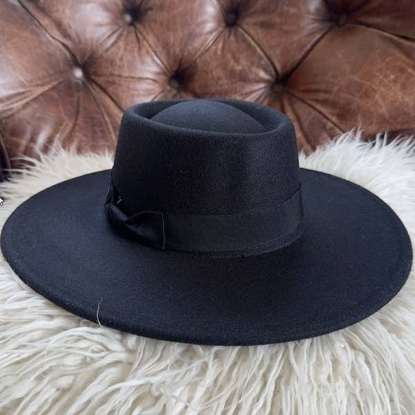 Black fedora hat on a fluffy white surface with a brown leather couch in the background