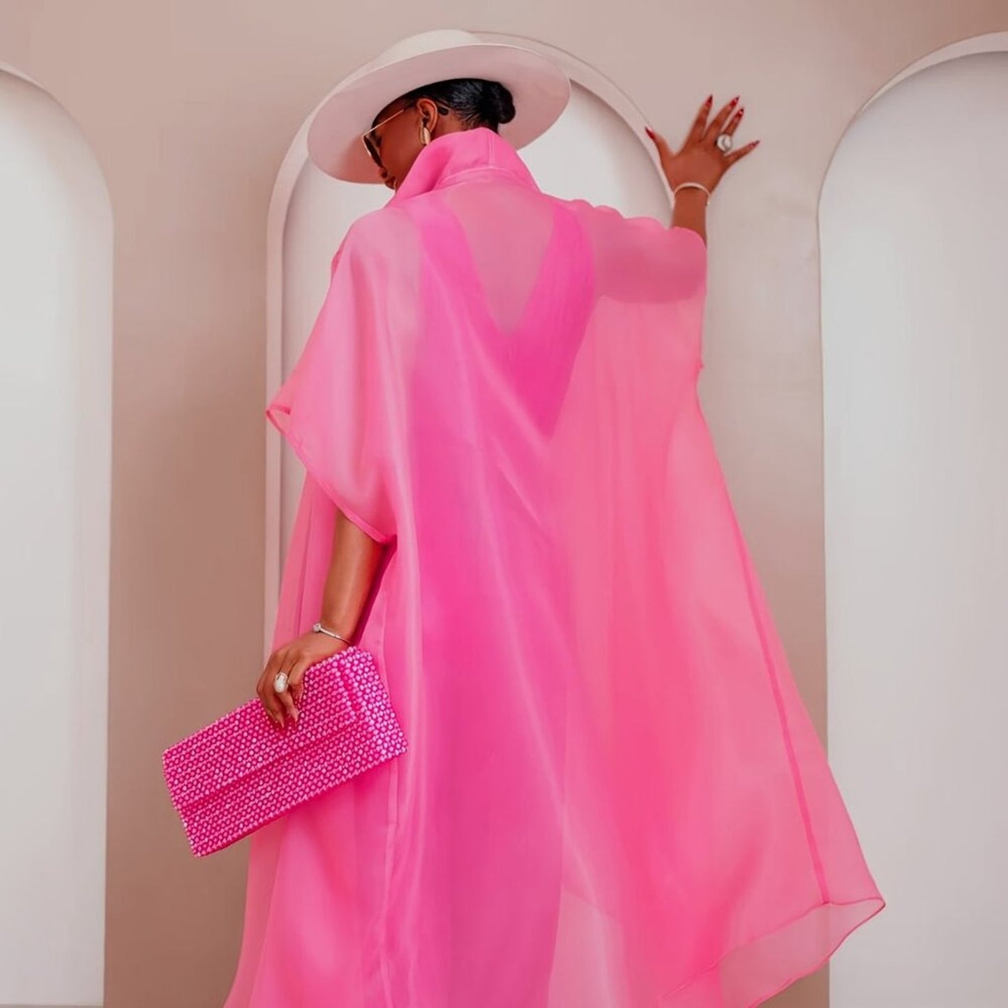 Person wearing a bright pink dress with a matching clutch in an archway.