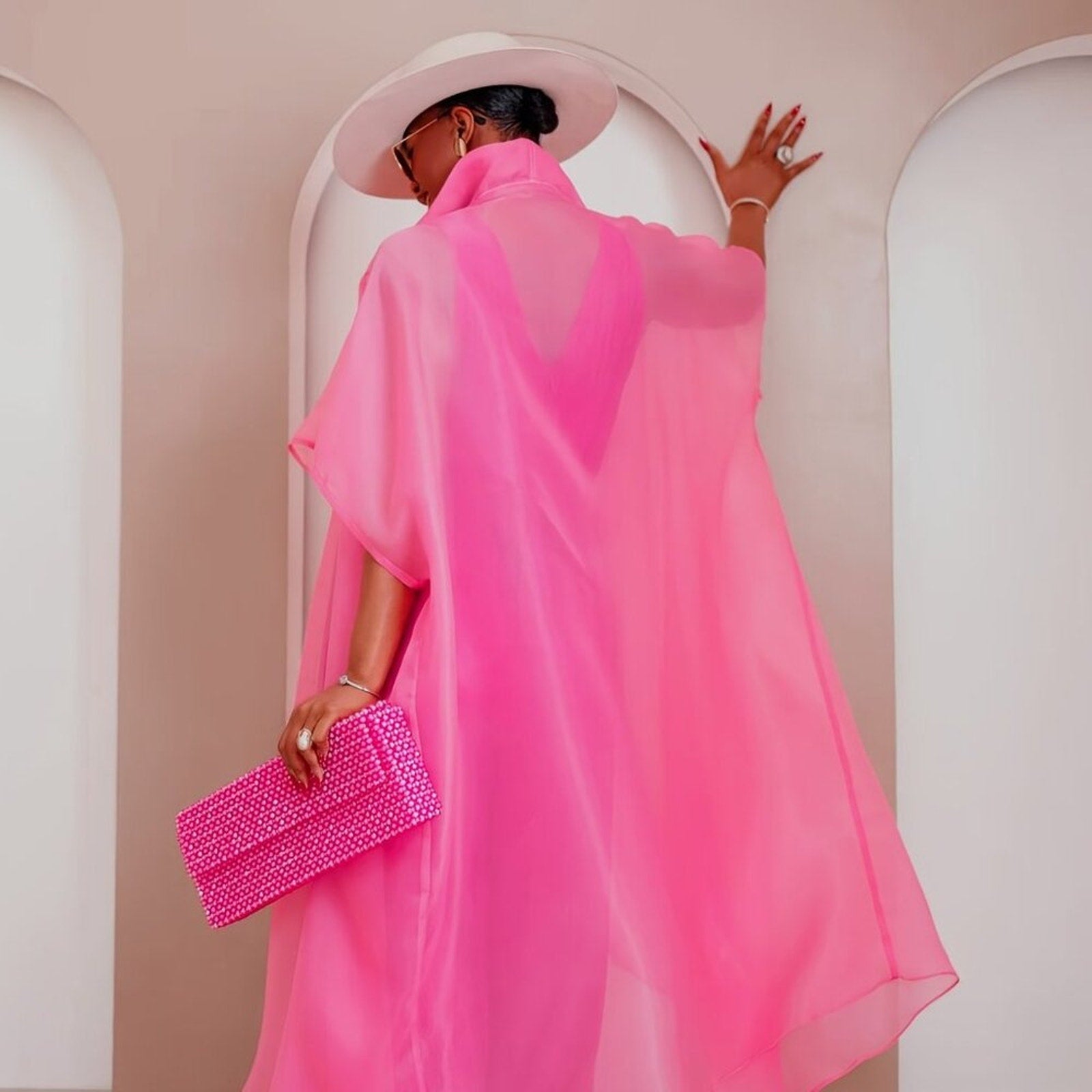 Person wearing a bright pink dress with a matching clutch in an archway.