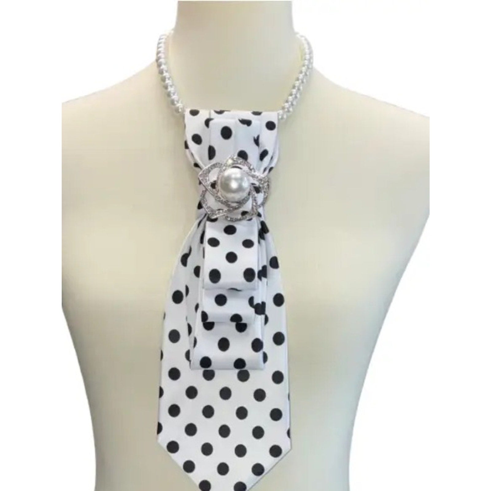 White mannequin wearing a black and white polka dot scarf with a pearl brooch on a white background