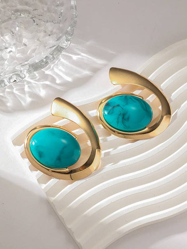 Gold earrings with turquoise stones on a textured white surface