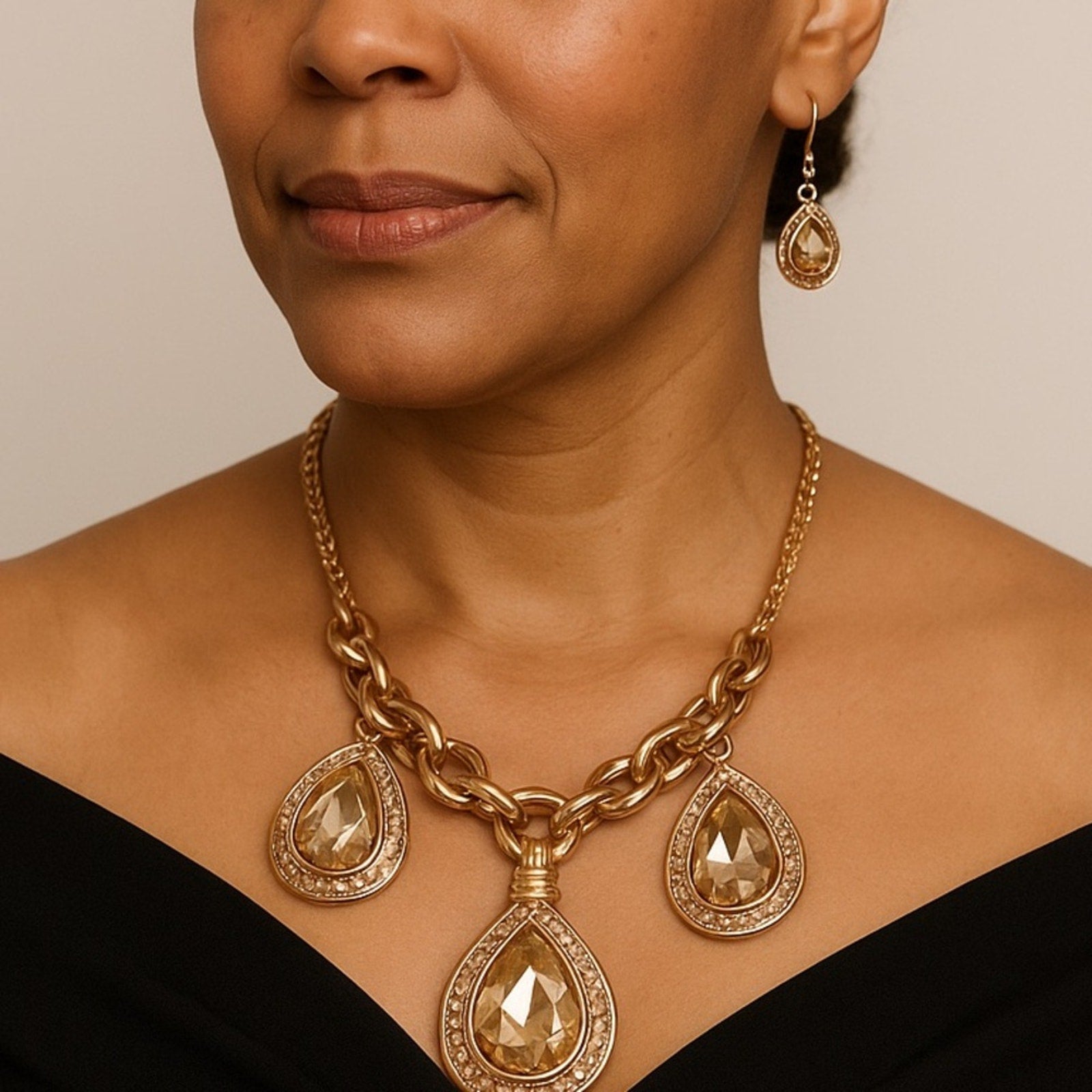 Woman wearing a gold necklace and earrings with teardrop pendants on a neutral background