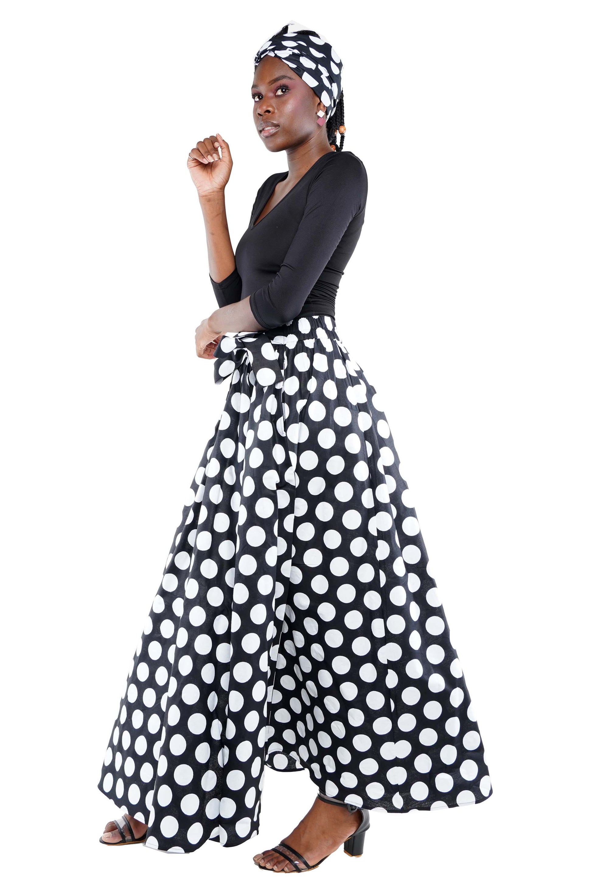 Woman wearing a black top and polka dot pants with a headscarf on a white background