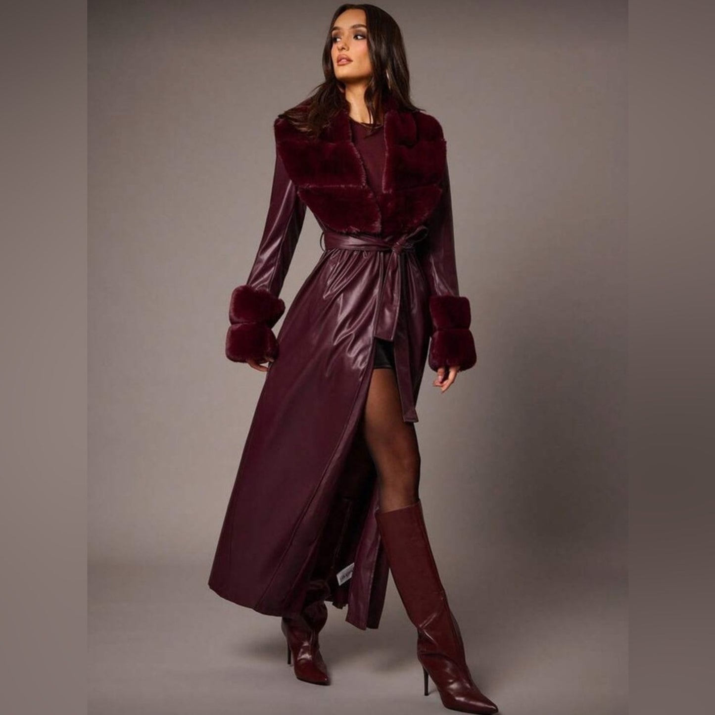 Woman wearing a burgundy coat with fur trim and matching boots on a gray background