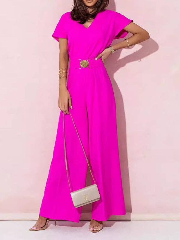 Person wearing a bright pink jumpsuit with a belt and holding a white handbag against a light pink background